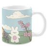 White ceramic 11oz mug featuring a charming spring scene with a cute white bunny holding a pink egg, surrounded by blooming pink cherry blossoms and purple flowers, set against rolling green hills under a soft blue sky with fluffy clouds.