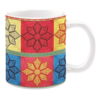 White ceramic mug featuring a colorful patchwork quilt design with intricate floral motifs in shades of red, yellow, blue, and black, framed with decorative borders, creating a bright and cheerful aesthetic.
