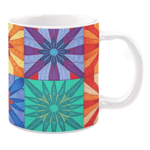 White ceramic mug featuring a colorful patchwork quilt design with bold flower patterns in vibrant shades of orange, purple, blue, and green, creating a lively and dynamic look.