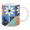 White ceramic mug featuring a patchwork quilt design with floral and geometric patterns in vibrant shades of orange, blue, green, and purple, creating a cozy and colorful aesthetic.