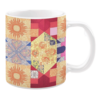 Colorful ceramic mug with quilt-inspired floral and geometric patterns in yellow, red, and blue tones