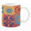 White ceramic mug featuring a colorful patchwork design with floral motifs in warm tones of red, orange, blue, and yellow, creating a vibrant and eclectic aesthetic.
